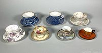 Seven cup-and-saucer pairs arranged on neutral backdrop