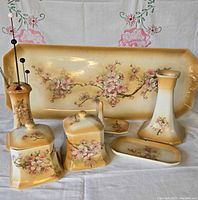 Front view showing all seven porcelain pieces on floral cloth backdrop