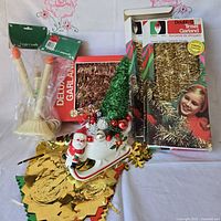 Group shot of all items: two garland boxes, candle lamp package, foil decorations pile, Santa sleigh assemblage