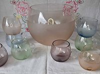 Punch bowl with seven pastel glasses displayed on cloth backdrop