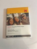 Front view of sealed Kodak Snapshot Photo Paper pack showing brand, size, finish, sheet count, and 180 GSM rating.