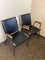 Front view of two black vinyl office chairs with chrome frames and wood arm caps