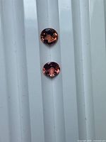 Two round radiant pink tourmalines aligned vertically on white ridged surface
