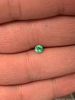 Round green emerald on fingertip