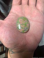 Front view of unakite cabochon in hand showing overall color and polish