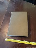 Front cover of olive green hardcover book with measuring tape showing approx 9 inches