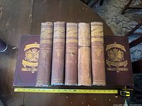 Seven volumes on table with tape measure for scale