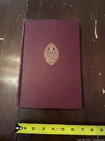 Front cover with gilt crest and measuring tape for scale