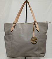 Front view of gray pebbled leather tote with MK charm and side pockets