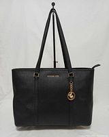 Front view of tote showing overall shape, straps, gold logo, charm