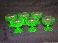 Six green uranium glass footed sherbet bowls on dark background