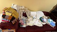 Sofa piled with afghans, crocheted throw, stacks of linens and doilies