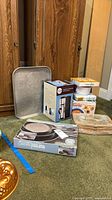 Boxed cast iron skillet set, stacked slow cookers, metal tray, glass casserole visible