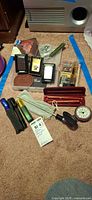 Group shot showing all items on carpet including lighters, flashlights, pen sets, watch, compass, goose call and tools