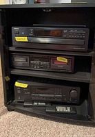 Front view of cabinet with components visible: CD changer, cassette deck, receiver, remotes