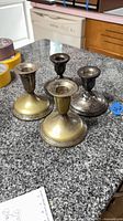Four small candlestick holders grouped on countertop: two silver-tone, two brass-tone