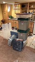 Group of seven plastic storage totes stacked with two packaged moving blankets