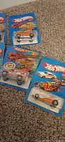Four carded Hot Wheels showing orange sports car, dragster, motocross van and silver racer