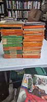 Full view of two tall stacks of vintage orange and green Penguin paperbacks on table