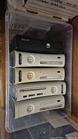 Stacked view of five Xbox 360 consoles in plastic bin