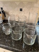 All eight clear glass vases and containers grouped on countertop