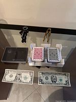 Group shot of all items: two playing card decks in foam holder and case, two novelty bills, keychain corkscrew, leg nutcracker