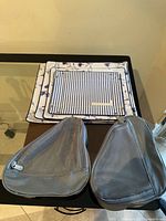 Two grey mesh shoe bags and stacked packing folders