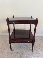 Full front view of the three-tier table showing trays closed and casters visible.