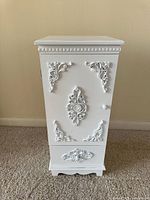 Front view of white cabinet showing ornate appliques