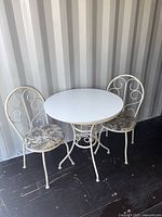 Full view of white metal round table with two matching chairs