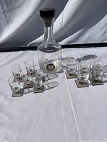 Full set showing decanter with stopper centered between two groups of five shot glasses on metal bases