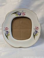 Front view of white ceramic frame with floral designs and opening
