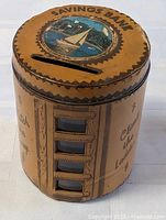 Full view of leather cylindrical bank showing top slot, sailboat graphic and side windows