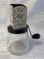full view of Androck nut chopper showing glass jar, metal lid, crank, patterned hopper
