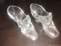 Pair of clear crystal glass boot figurines on dark surface
