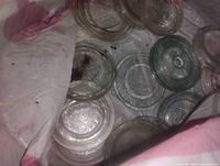 Bag containing multiple clear and light aqua glass sealer tops