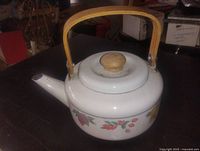Side view of white enamel metal teapot with floral pattern and bamboo handle
