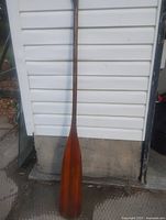 Full view of wooden paddle leaning against siding, shows entire item