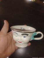Front of Baileys ceramic winking face teacup showing facial features and bow handle