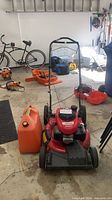 Front and side view of red Troy-Bilt lawn mower with handle folded and orange gas can