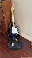 Full view of blue Ibanez Stagestar guitar leaning against wall with gig bag, strap and picks