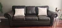 Front view of brown leather sofa with two floral cushions