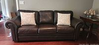 Front view of brown leather sofa with two floral pillows
