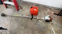 Full view of trimmer and red gas can on garage floor