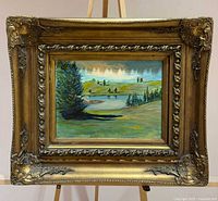 Full view of framed painting on easel showing ornate gilt wood frame and landscape artwork