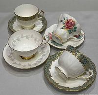 Five teacups and saucers arranged to show patterns and gilt trim