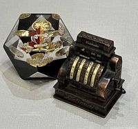 Both items side by side: acrylic penny paperweight and miniature cash register sharpener