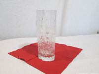 Full view of clear textured glass vase on red cloth