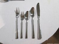 Five-piece place setting showing knife, dinner fork, salad fork, tablespoon, teaspoon