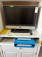 Front view of Daenyx 26" LCD TV on stand with remote, manuals and boxed DVP-6100 DVD player